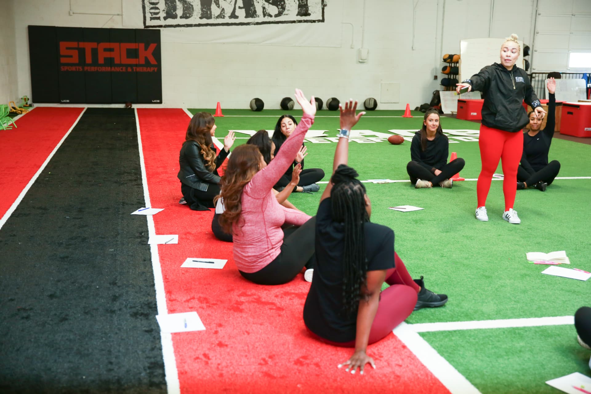 Members seated on the turf raising their arms during the guided stretch at STACK Sports Performance