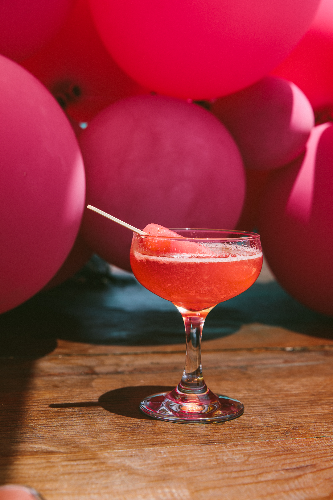 Watermelon cocktail in a coupe glass against a wall of pink balloons