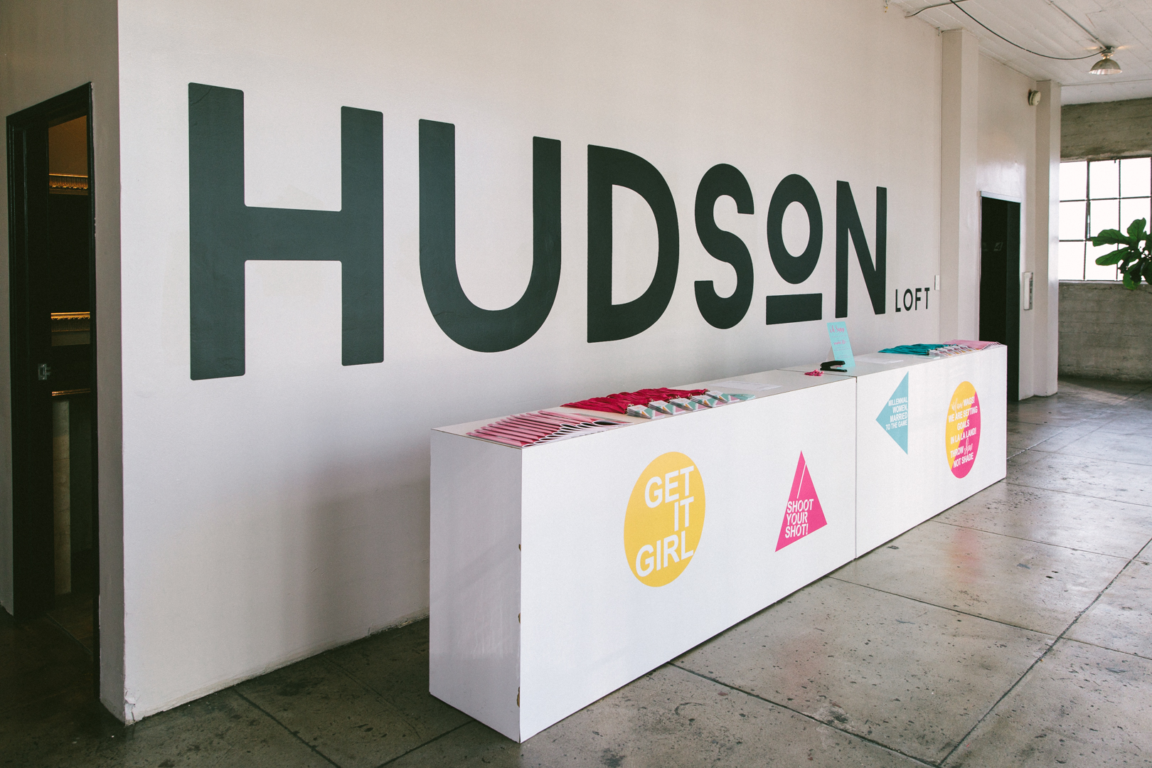 Hudson Loft check-in table set with lanyards and GET IT GIRL signage under the HUDSON mural