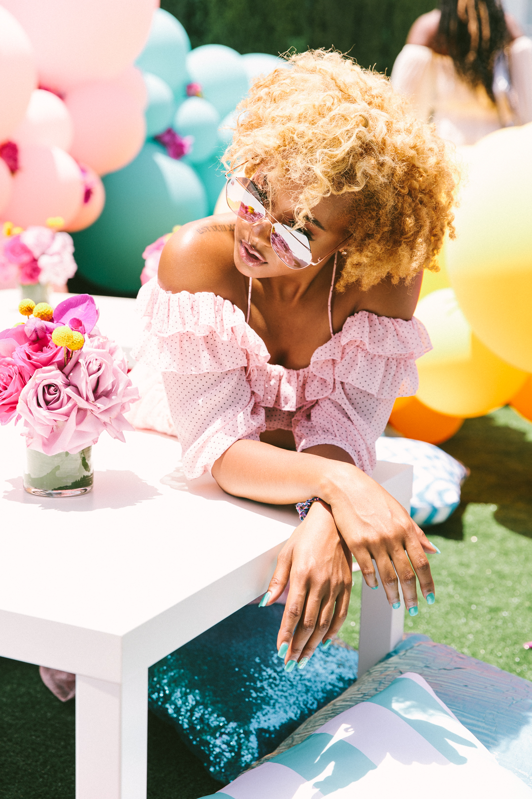 Guest in a pink ruffled top lounging at the rooftop tables beside the balloon wall