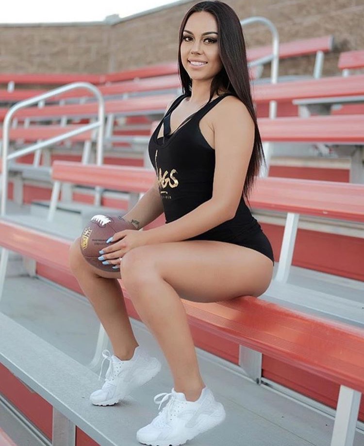 Member in a WAGS Redefined bodysuit seated on stadium bleachers holding a football