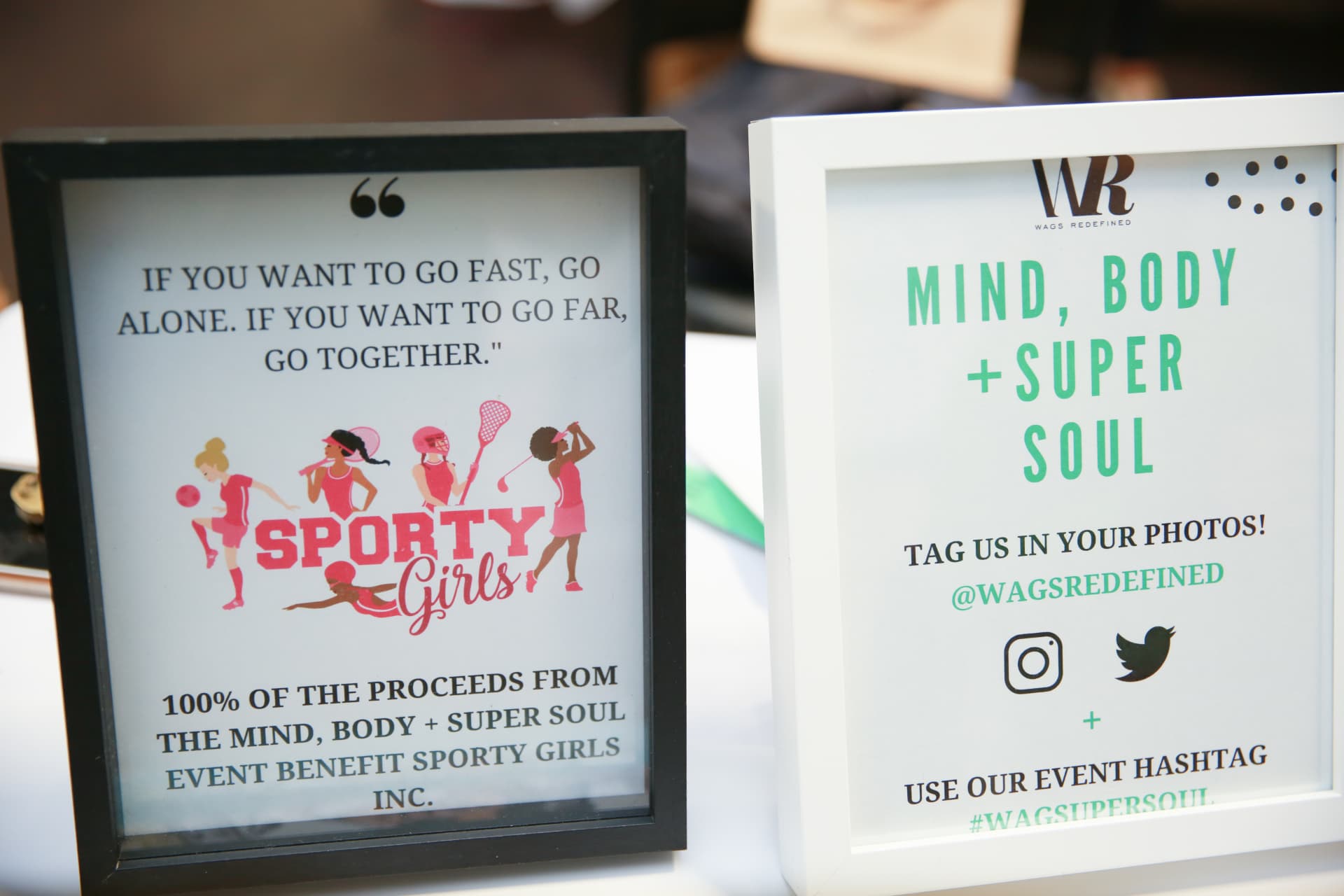 Signage noting 100% of event proceeds benefit Sporty Girls Inc. beside the event hashtag card