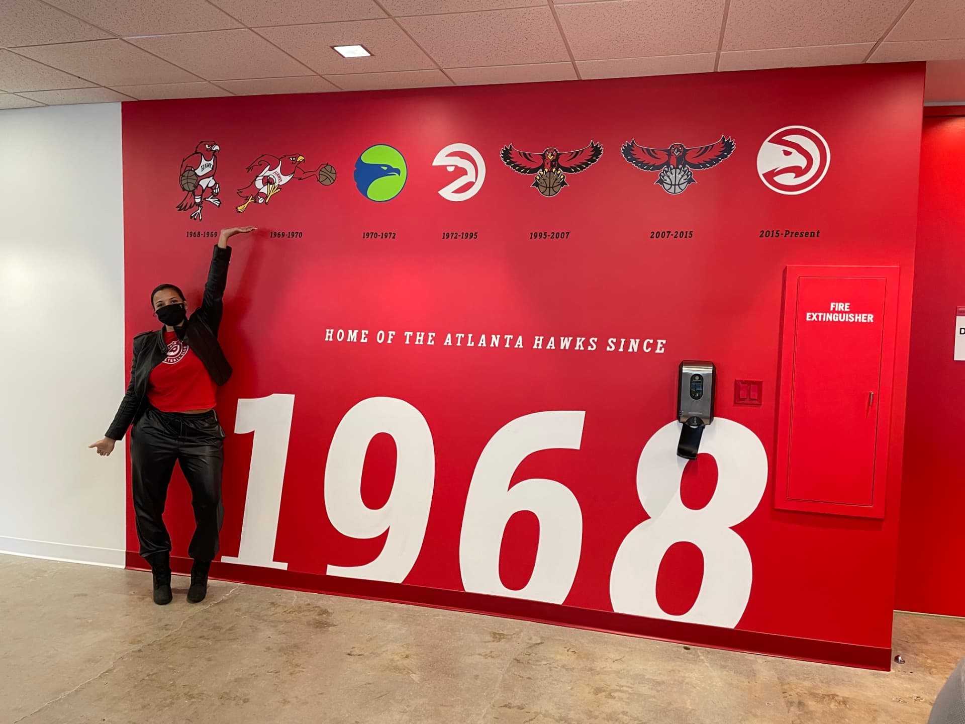 LeLe Martin next to the Atlanta Hawks logo history wall reading 'Home of the Atlanta Hawks since 1968' at State Farm Arena