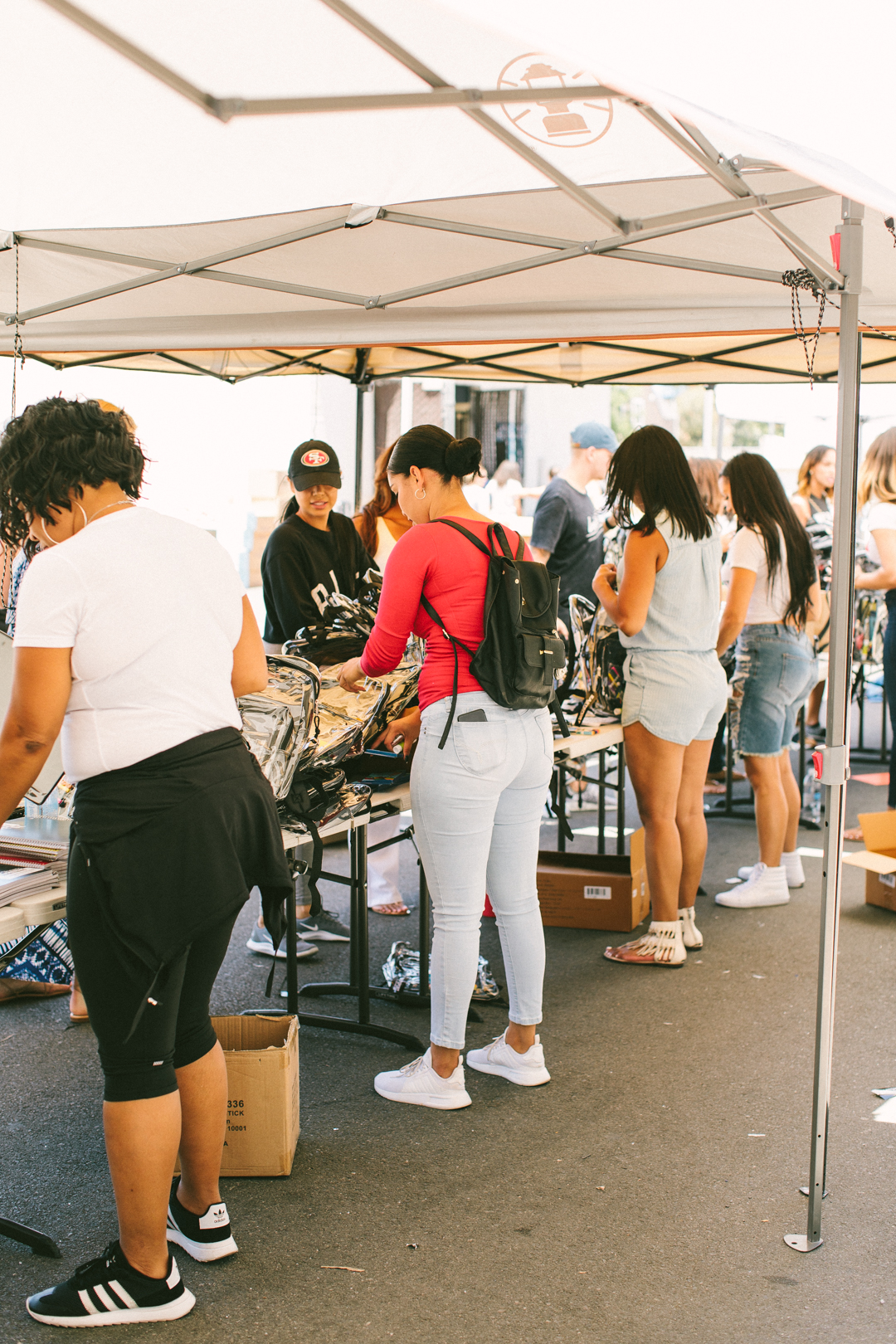 Volunteers and students working the backpack distribution line under the canopy