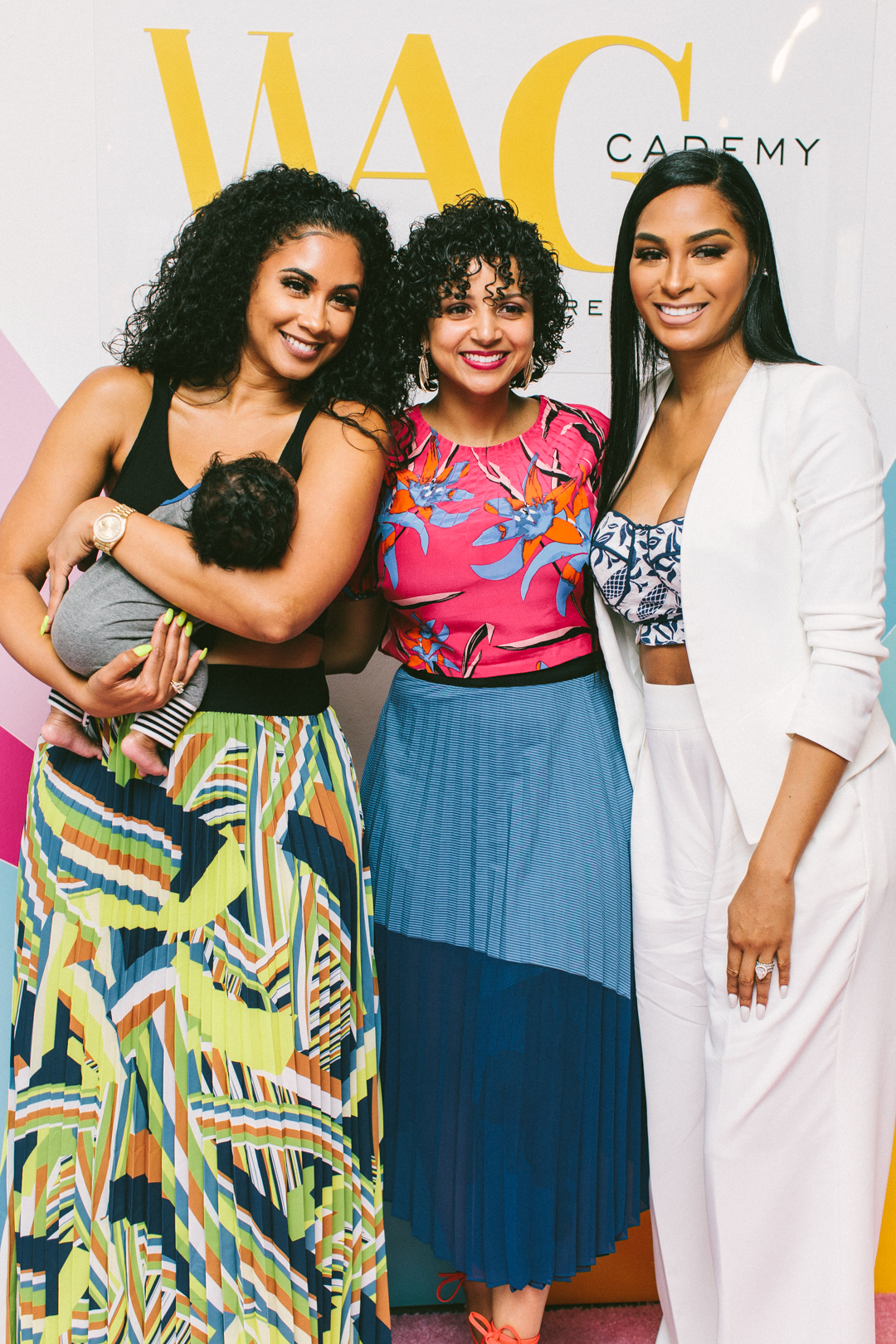 Three attendees, one holding her baby, posing on the WAGcademy step-and-repeat