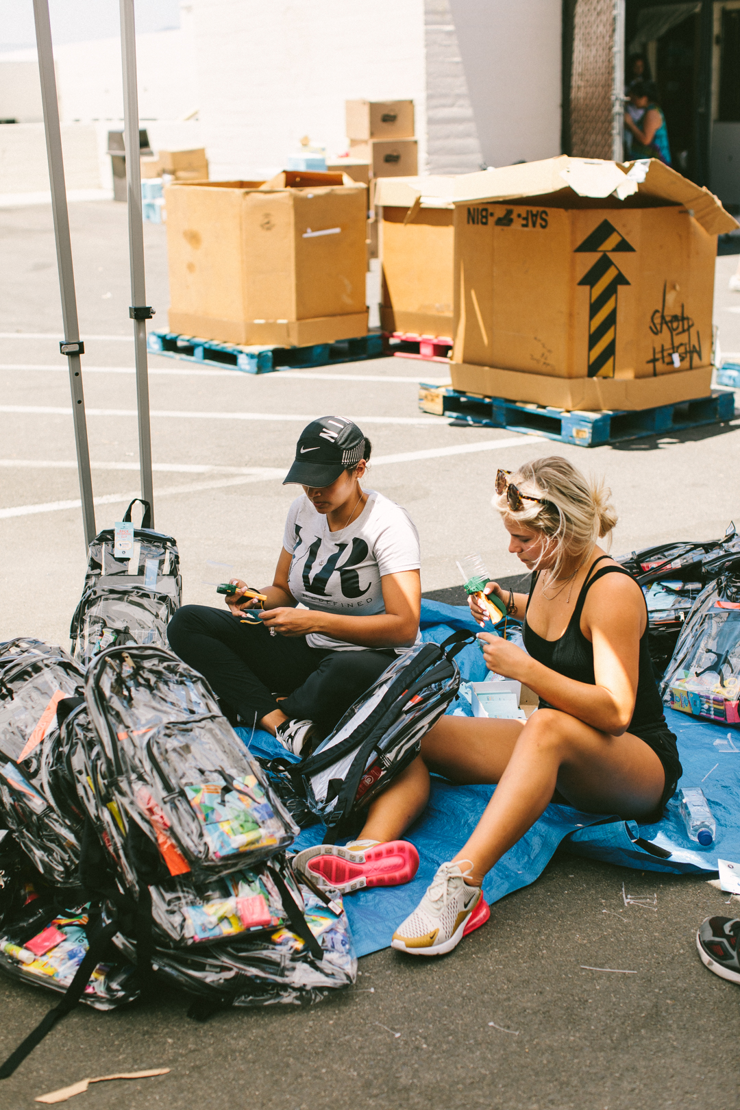 Two members seated on a tarp packing clear backpacks with school supplies