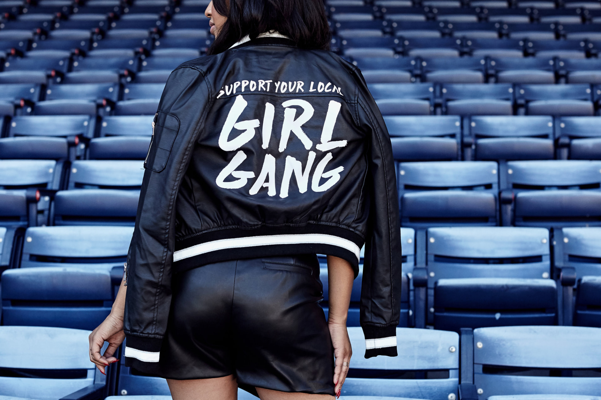Woman in a stadium wearing a 'Support Your Local Girl Gang' leather jacket