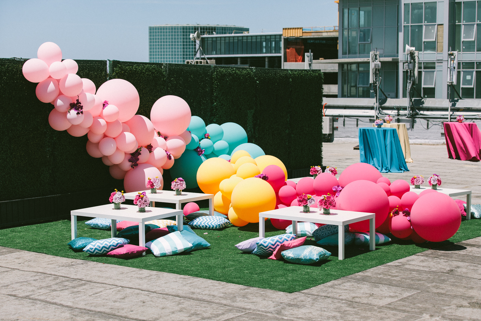 Rooftop lounge with a pink-to-teal balloon installation, low tables and floor cushions