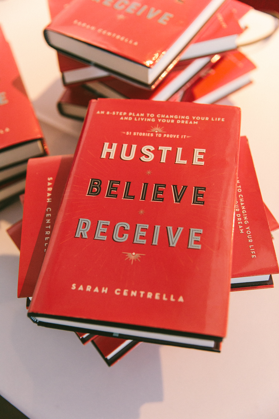 Stacked copies of Hustle, Believe, Receive on the WAGcademy welcome table